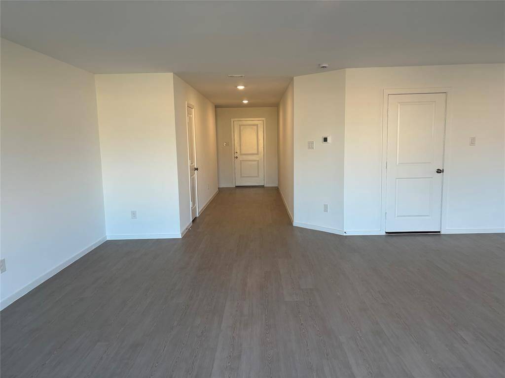 This photo shows a spacious, family room with light-color walls and wood-style flooring. It features a hallway leading to entrance and creating an open and inviting layout.