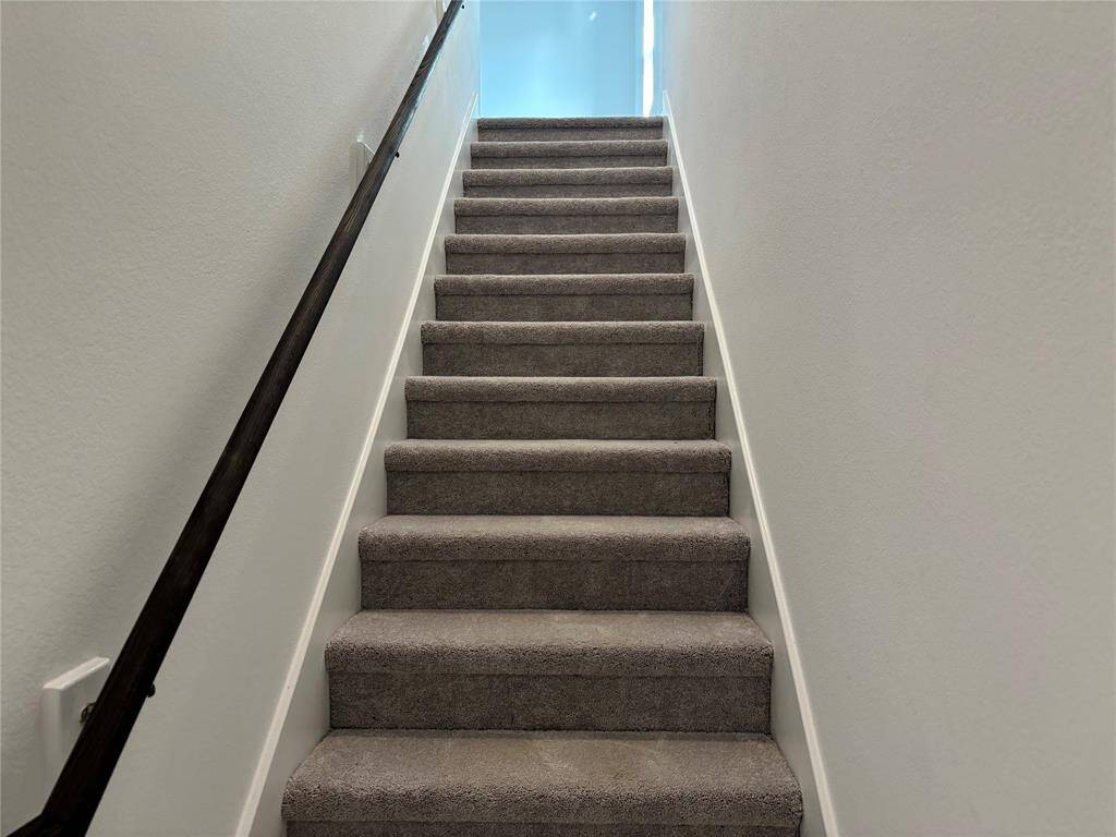 This photo shows a carpeted staircase with a simple, sleek handrail, leading to an all 4 rooms and game room at upper level. The walls are painted in a neutral color, providing a clean and modern look.