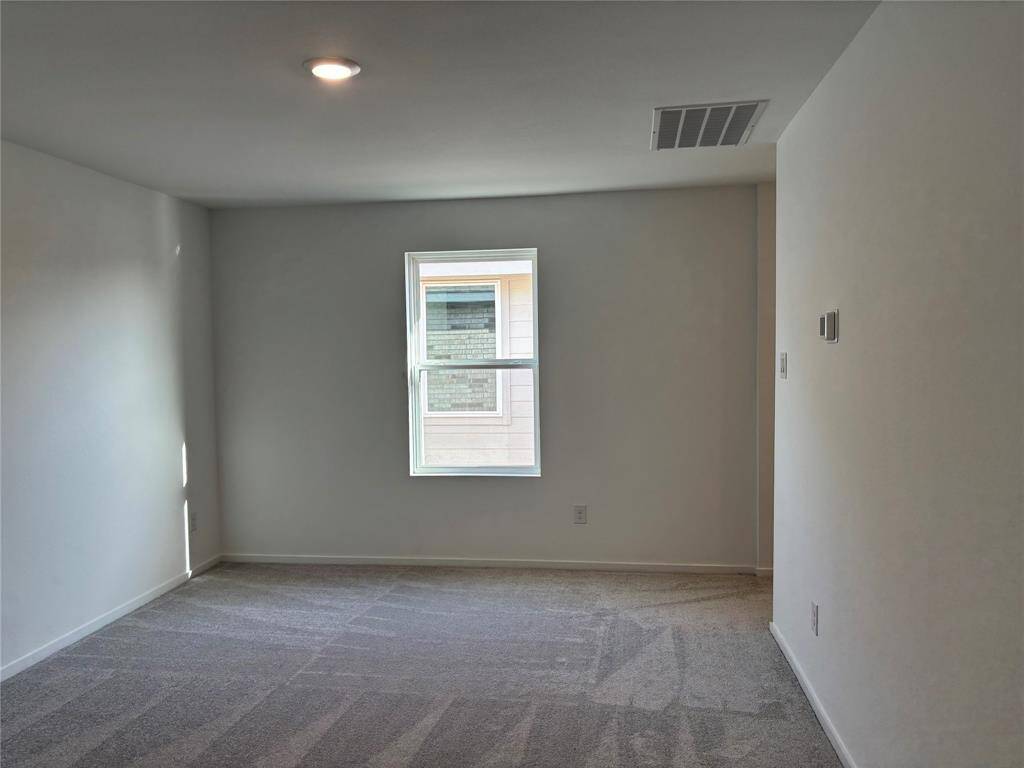 This game room features neutral-color walls and carpet, a single window for natural light, and a recessed ceiling light, creating a simple and bright space.