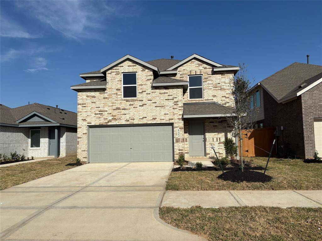 This photo showcases a modern two-story brick house with a two-car garage. The front yard features a small lawn and newly planted shrubs, all set against a clear blue sky.