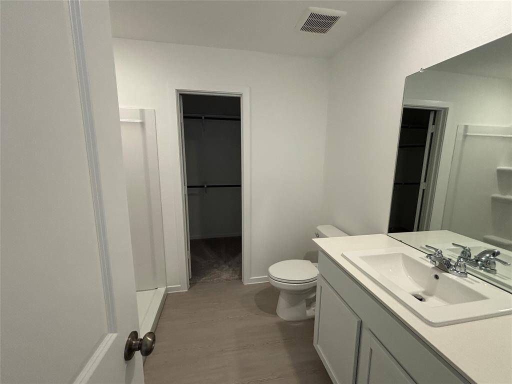 This is a modern primary bathroom with a sleek design, featuring a large mirror, single sink vanity, toilet, and a walk-in shower. The space is bright with neutral tones, offering a clean and open feel.