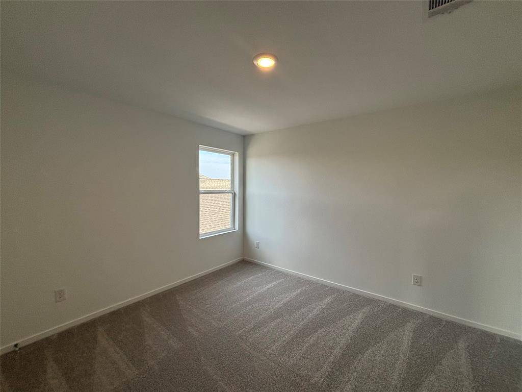 This is a second bedroom bright, carpeted with neutral walls, a single window providing natural light, and a ceiling light fixture, ideal for a bedroom or office.