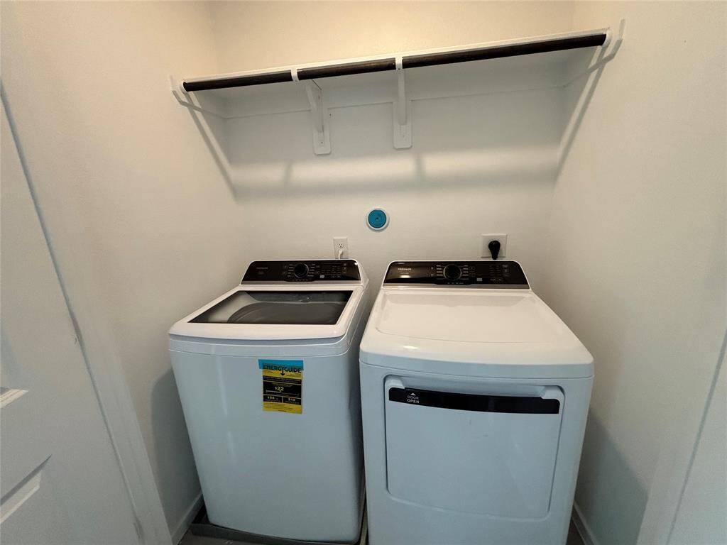 This photo shows a compact laundry area with a modern washer and dryer set beneath a white shelf, ideal for organizing laundry supplies.