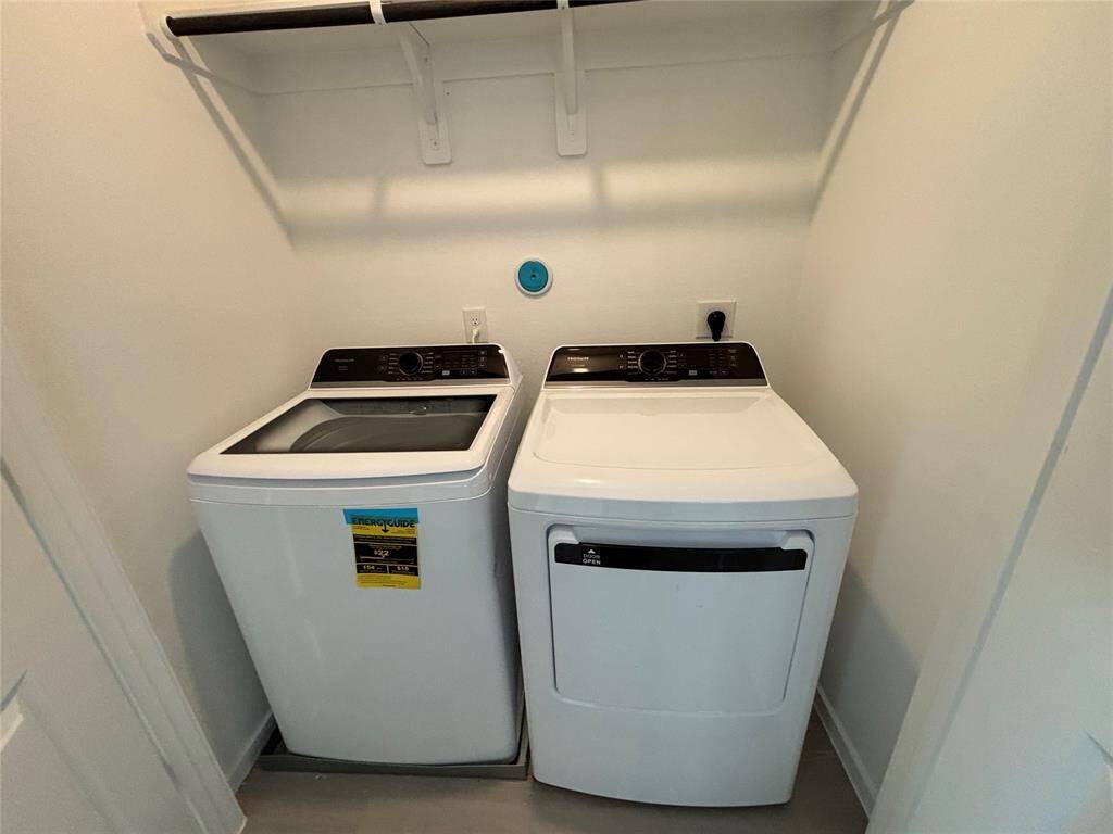 Compact laundry area featuring a top-loading washer and dryer, with a shelf above for storage. Ideal for efficient use of space.