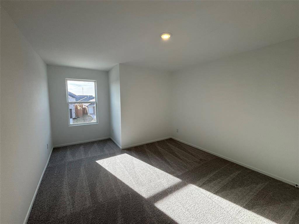 This 3rd bedroom is bright and spacious with neutral walls and carpet, featuring a single window that allows natural light to fill the space.