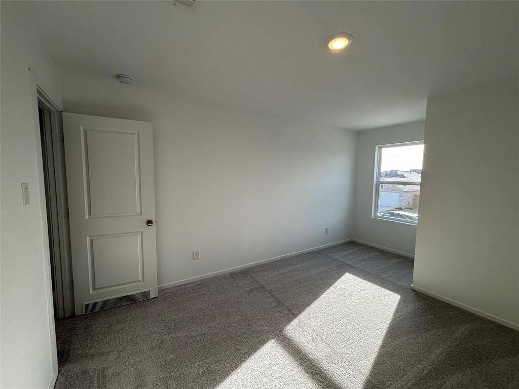 This is a 4th bedroom bright, carpeted room with neutral walls, featuring a window that lets in natural light and a closed door. It offers a clean, blank canvas for personalization.