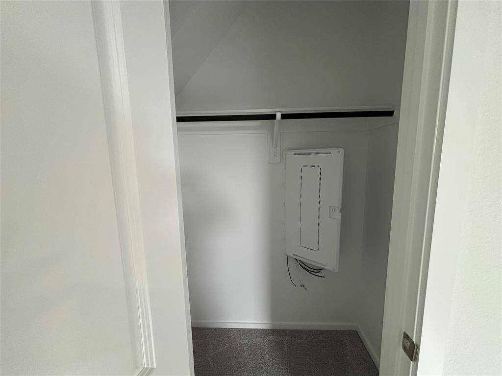 This photo shows a small, white-painted closet with carpeted flooring. It features a mounted electrical panel and a single shelf with a hanging rod. Ideal for additional storage.