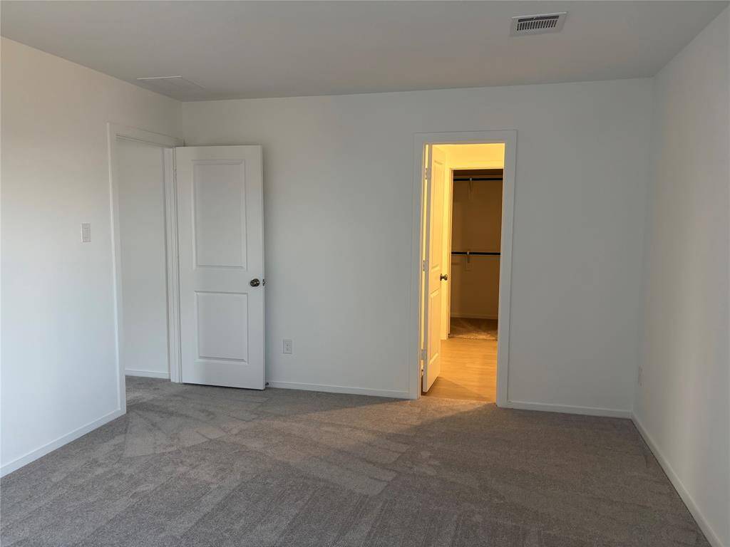 This is a bright, empty bedroom with neutral walls and carpet. It features a door leading to a well-lit walk-in closet. The room is simple, offering a blank canvas for personalization.