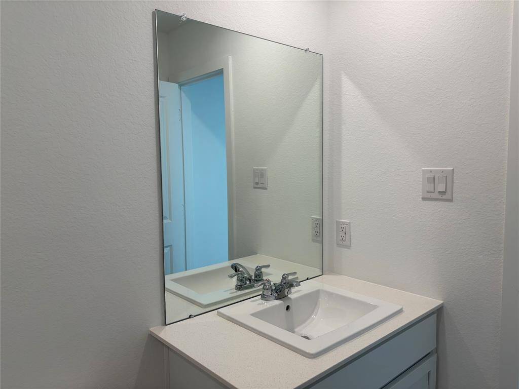This secondary bathroom features a clean, modern design with a large mirror above a sleek white vanity. The countertop includes a built-in sink and contemporary faucet, complemented by neutral wall tones.