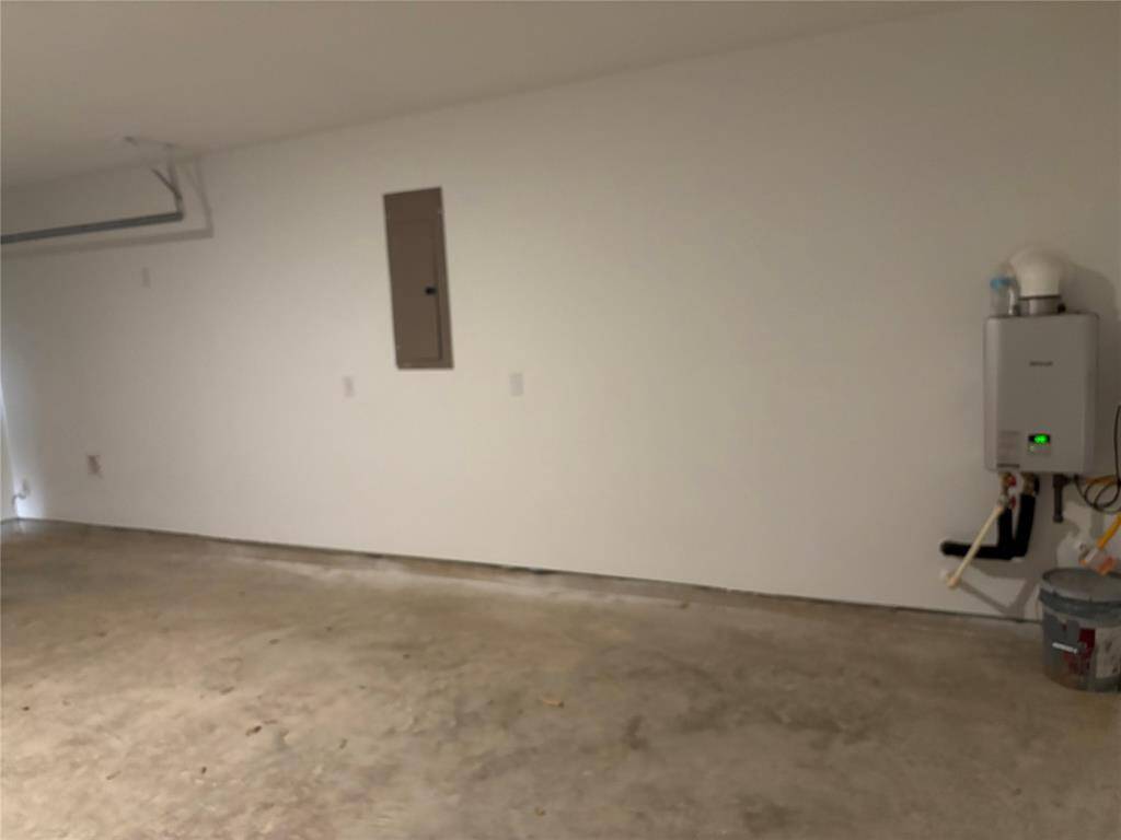 This is a clean, spacious 2 car garage with a concrete floor and a white wall. It features a mounted tankless water heater and an electrical panel, offering utility and storage potential.