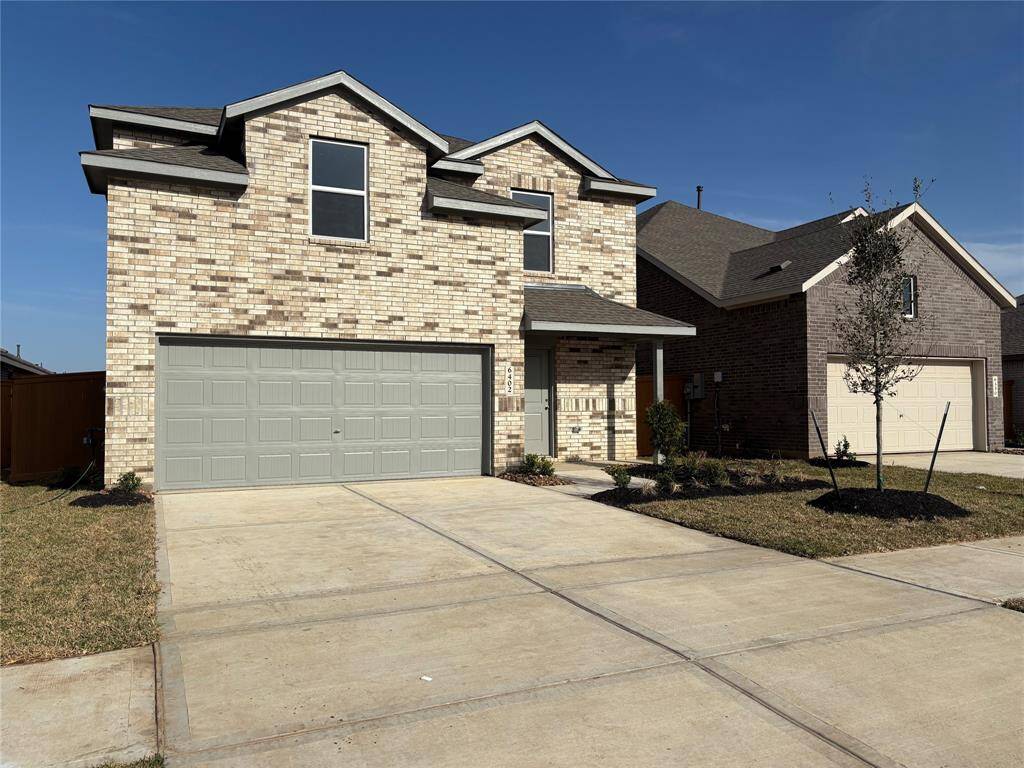 This is a modern, two-story brick home with a spacious two-car garage. The exterior features a clean, contemporary design with a landscaped front yard and a wide driveway, offering ample parking space.