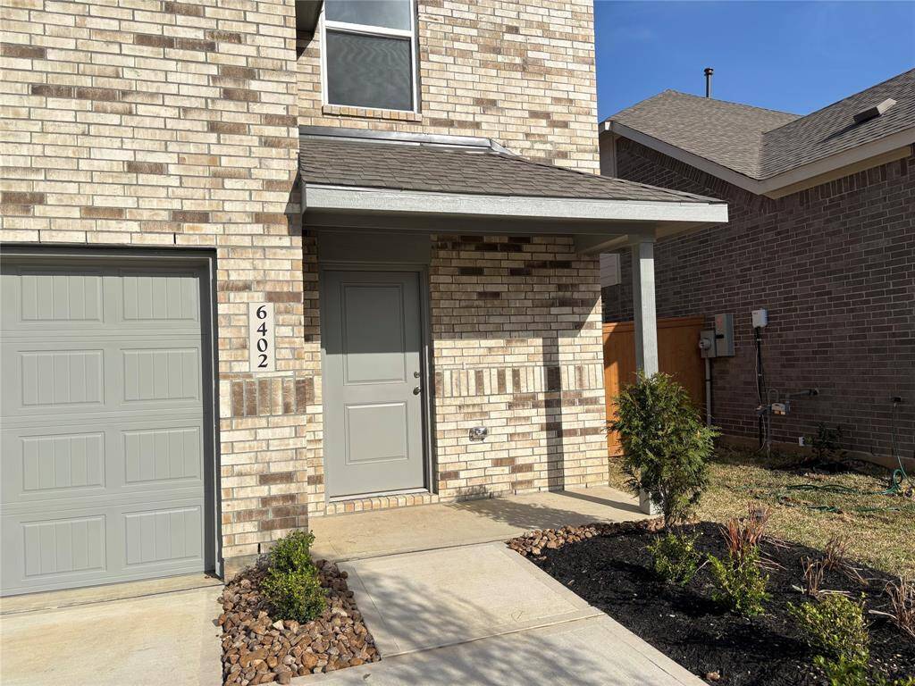 Modern two-story home with a light brick exterior, featuring a two-car garage and a cozy front entrance. The yard is landscaped with small shrubs and a neat walkway.