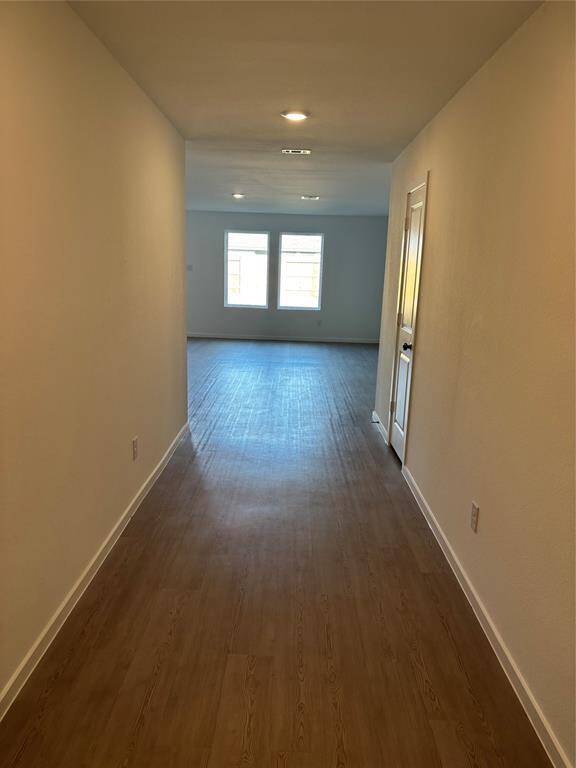 A bright, long hallway with Luxury Vinyl flooring leads to a spacious room with two large windows, providing natural light.