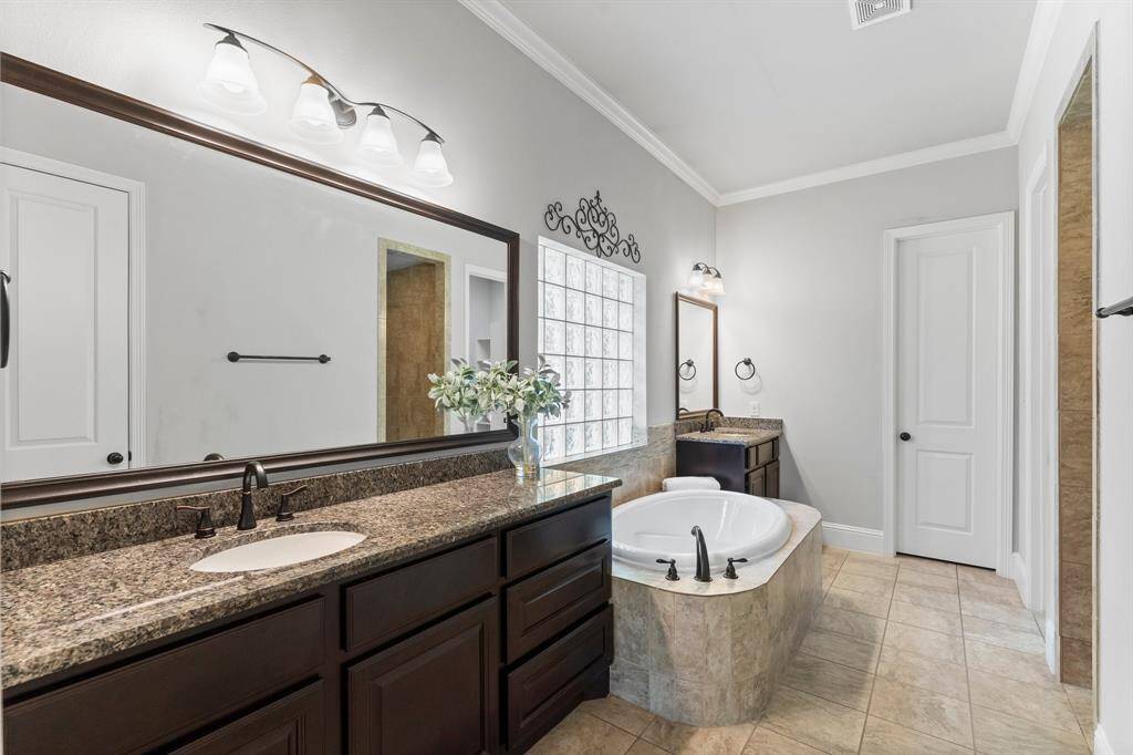Primary bath features dual sinks, granite countertops, and dark wood cabinetry. elegant tile flooring, offering a luxurious and relaxing atmosphere.