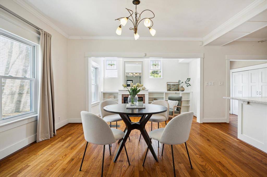 An open concept dining room with views toward the updated kitchen. Light flows through multiple windows, reflecting off the warm wood floors and light-toned walls.