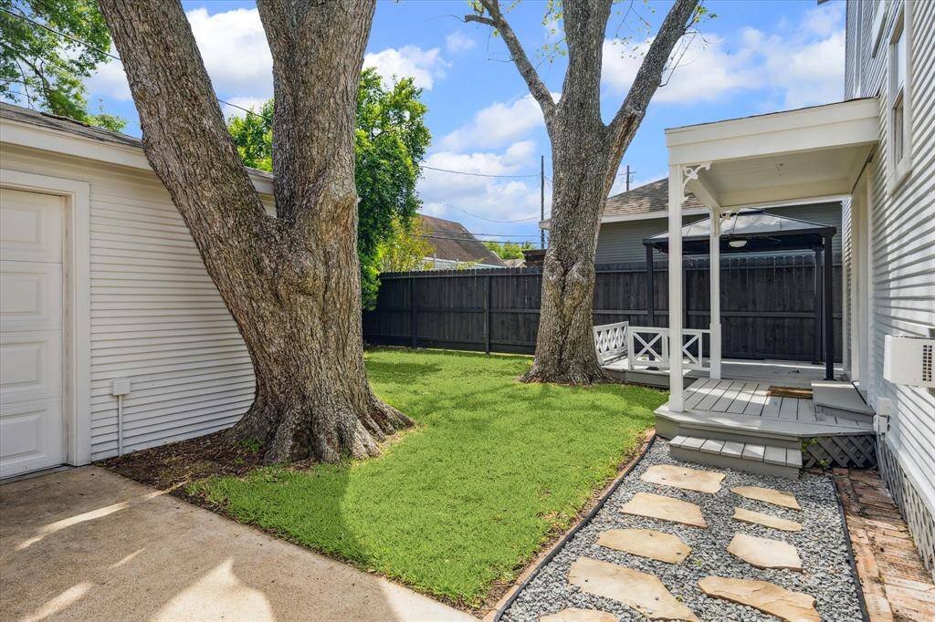 Fenced backyard with grassy space, mature shade trees, and a path leading to the deck. A private outdoor area with room to play or relax.