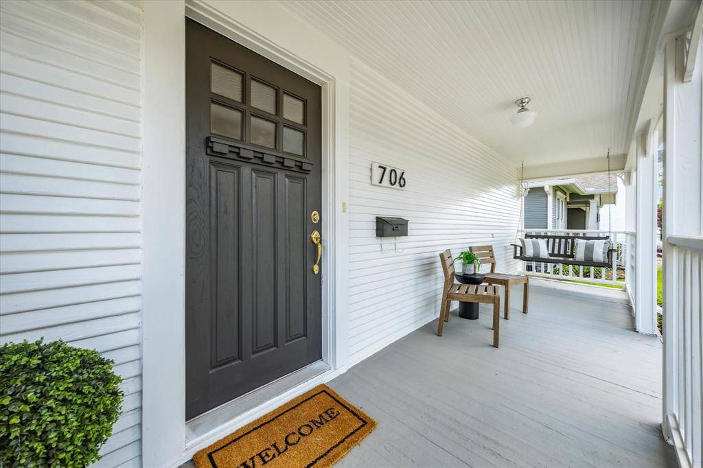 A close-up of the classic front door with a “Welcome” mat, white beadboard ceiling, and the home’s address plate, setting the tone for timeless hospitality.