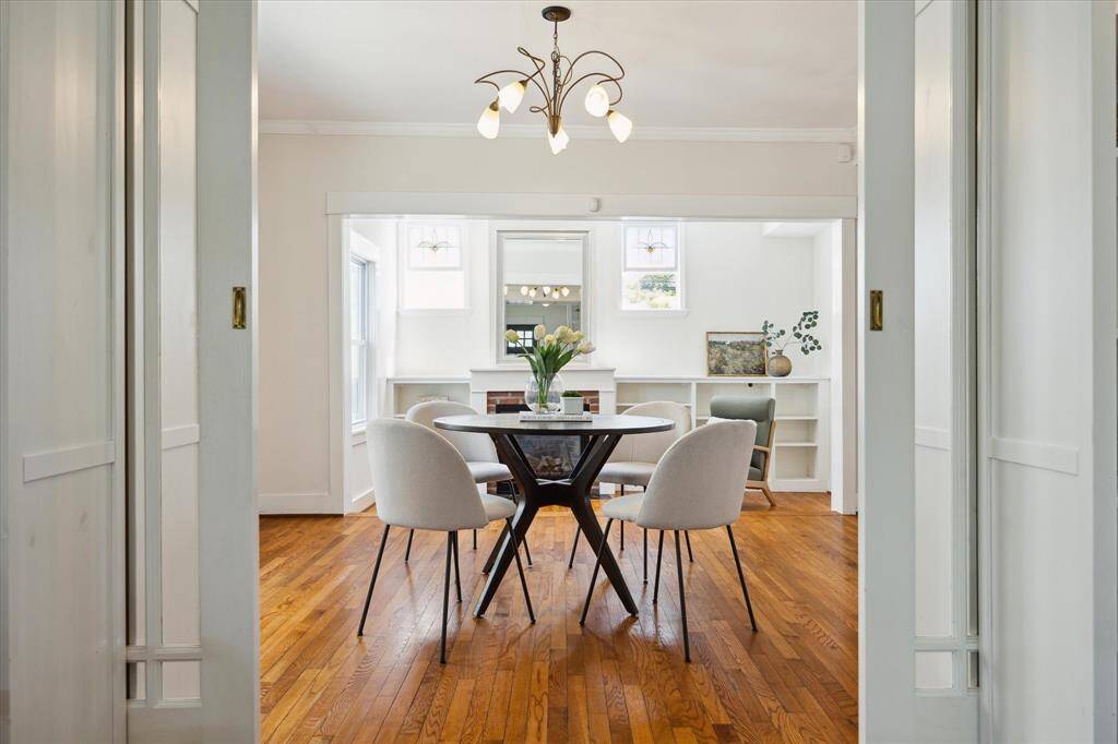 A crisp view through double pocket doors into the dining area, featuring mid-century modern furnishings and built-in bookshelves, anchored by glowing hardwood floors.