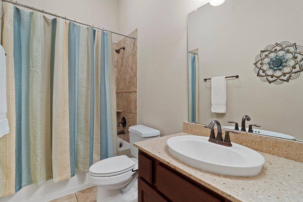 This en suite bathroom boasts a shower/tub combo, a vanity with a granite countertop, and a convenient linen closet.