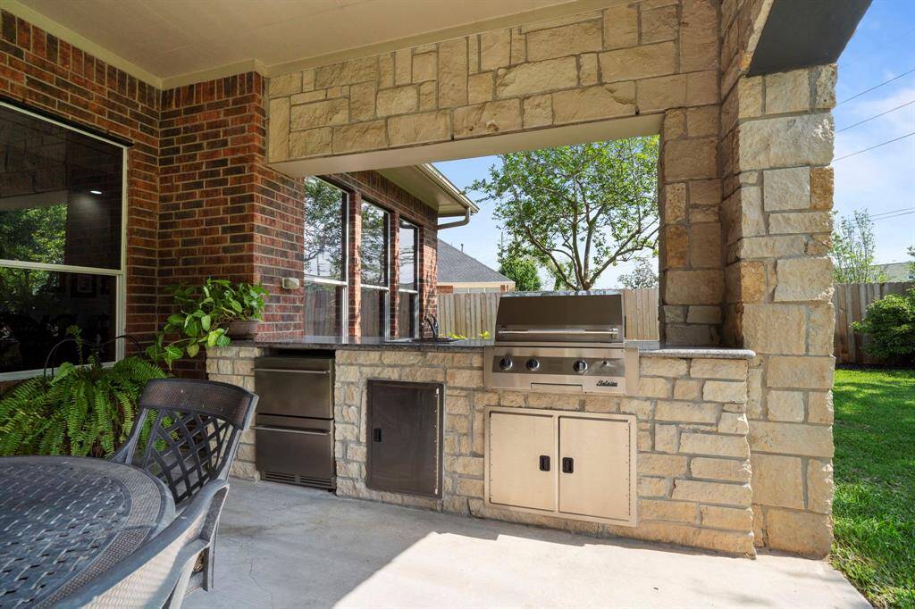The outdoor kitchen features a gas grill connected to the main gas line, a full-sized stainless steel sink, mini-fridge, storage cabinets, and a sleek Silestone countertop.