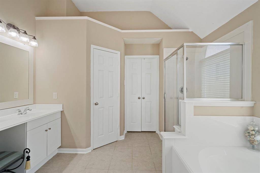The spacious en suite bath features a dual vanity, a luxurious jetted tub, a glass walk-in shower, a private water closet, and a walk-in closet.