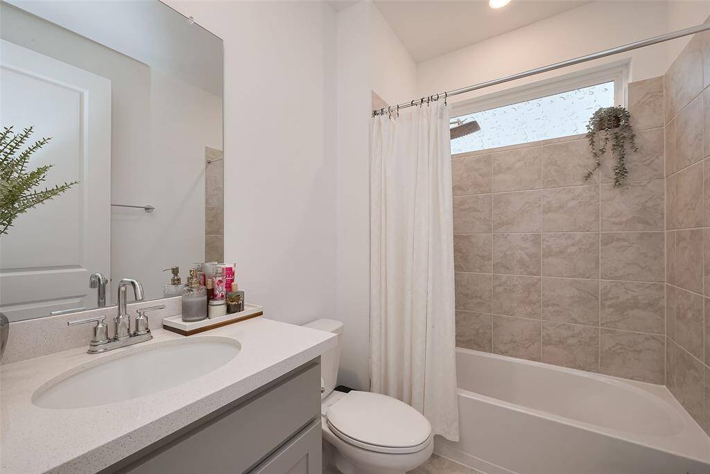 Modern bathroom next to the front bedroom featuring elegant tilework, a sleek vanity, and a spacious tub with a shower.