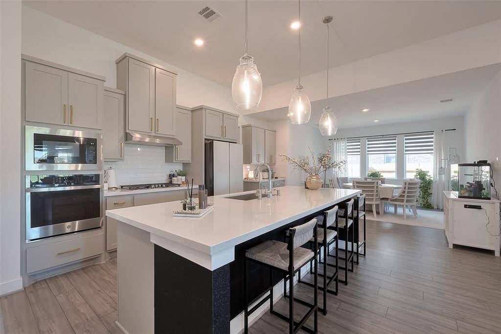 This modern kitchen features sleek cabinetry, stainless steel appliances, and a large island with seating. The open layout flows into a bright dining area with large windows, creating a welcoming space for entertaining.