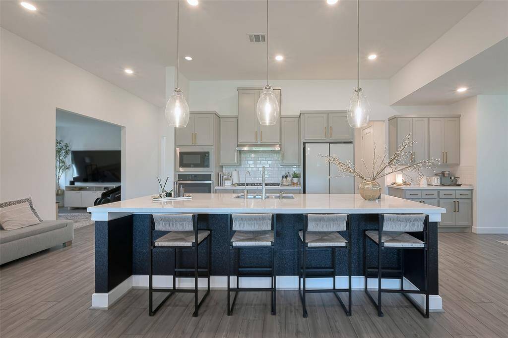 This modern kitchen features sleek cabinetry, a spacious island with seating for four, and stylish pendant lighting. It opens into a cozy living area, creating an inviting space for entertaining.