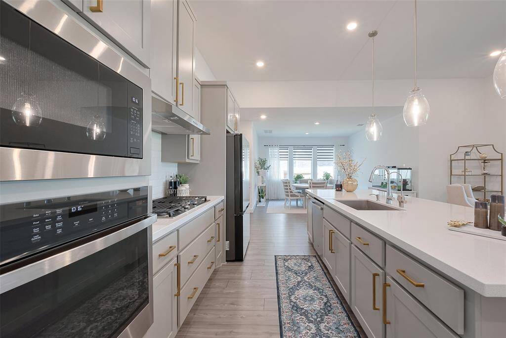 This modern kitchen features sleek stainless-steel appliances, ample white cabinetry with gold handles, and a spacious island with pendant lighting. The open layout flows into a bright and huge dining area, creating a perfect space for entertaining and family gatherings.