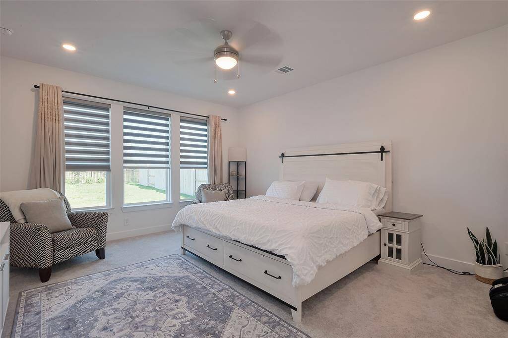 Spacious primary bedroom with abundant natural light, featuring a cozy sitting area and modern ceiling fan.