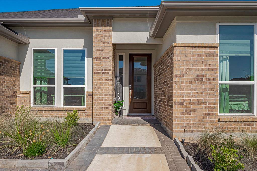 Experience modern elegance at this home's entrance, featuring a striking blend of brick and light siding. Large windows flood the interior with natural light, while a charming pathway guides you to the inviting front door.