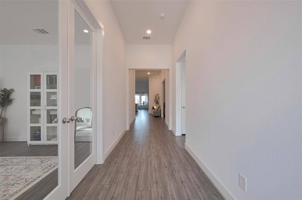 Bright and spacious hallway with modern wood flooring, leading to multiple rooms. Features glass double doors on the left, enhancing natural light and openness.