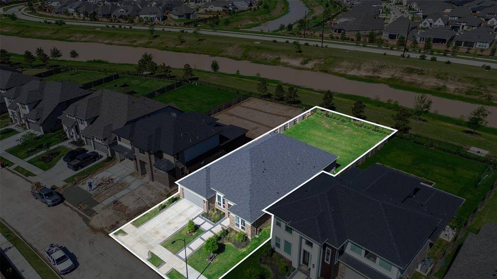 This photo showcases a modern, spacious home with a large backyard, outlined for clarity. It’s located in a suburban neighborhood near a waterway, offering a peaceful and scenic environment. The property features a well-maintained driveway and is surrounded by similar stylish homes.