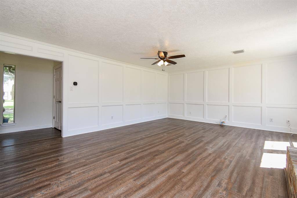 This spacious living room features elegant white wainscoting and rich luxury vinyl flooring. Large windows allow natural light to fill the room, enhancing its welcoming atmosphere.