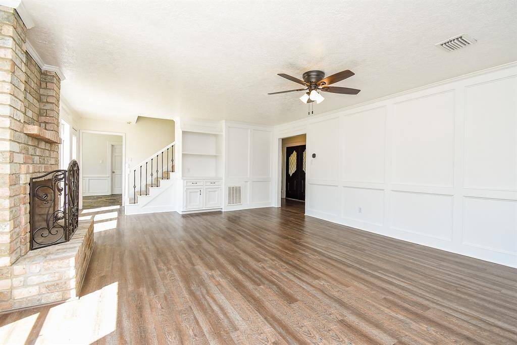 This spacious living area features hardwood floors, a brick fireplace, and a ceiling fan. It has built-in shelving and a view of the staircase, offering a bright, open layout that’s perfect for family gatherings.