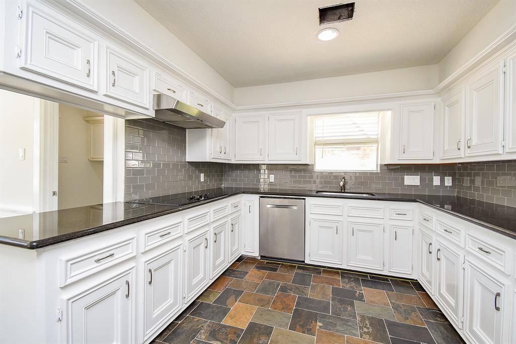 This kitchen features white cabinetry, dark granite countertops, and gray subway tile backsplash. It includes modern stainless steel appliances and a multi-toned tile floor, offering a clean and spacious look.