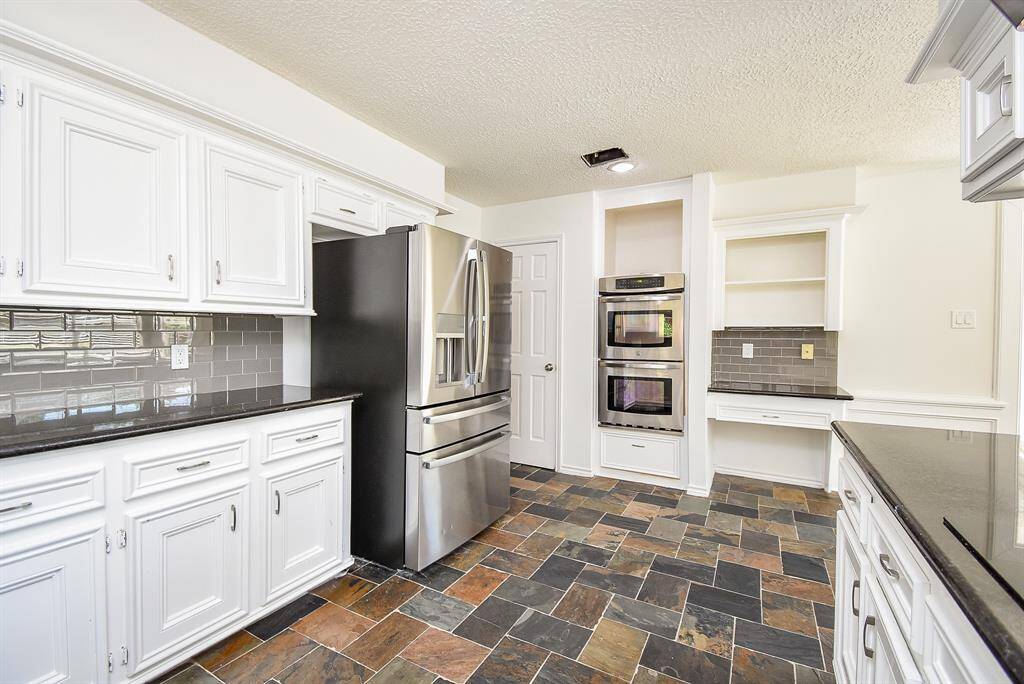 Spacious kitchen with modern stainless steel appliances, sleek black countertops, and classic white cabinetry. The room features a double oven, a stylish tiled backsplash, and a unique slate floor, offering a blend of function and style.
