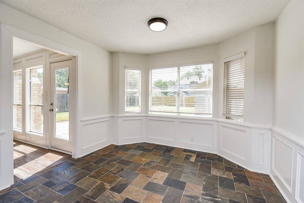 Bright breakfast area with large windows, tile flooring, and white wainscoting. Access to outdoor space.