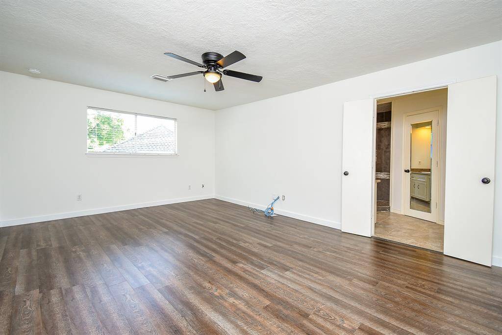 Spacious Primary bedroom with luxury vinyl flooring, and ample natural light from a large window. It connects to an updated ensuite bathroom, featuring modern fixtures and tiled flooring.