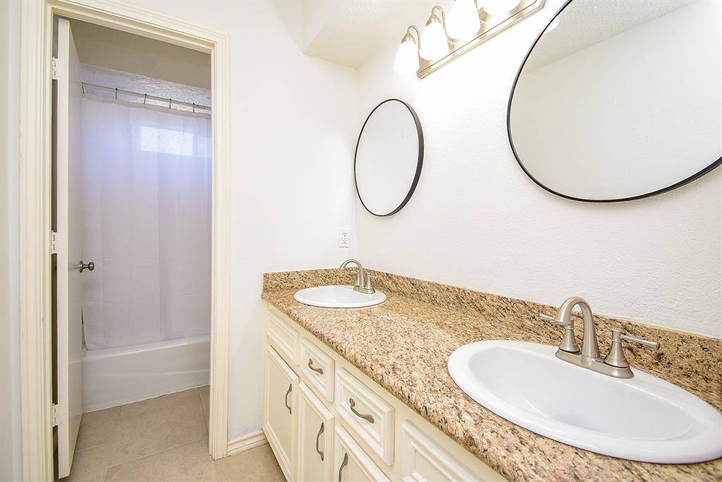 Secondary bathroom features a double vanity with granite countertops, modern mirrors, and fixtures. It has a bathtub with a shower and a neutral color scheme for a clean, bright look.