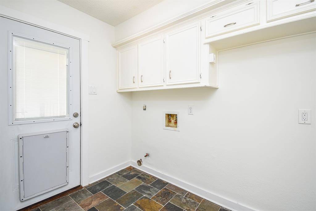 This photo shows a utility room with white cabinets for storage, a door with a pet flap, and a tiled floor. It's a practical space for laundry or storage needs.