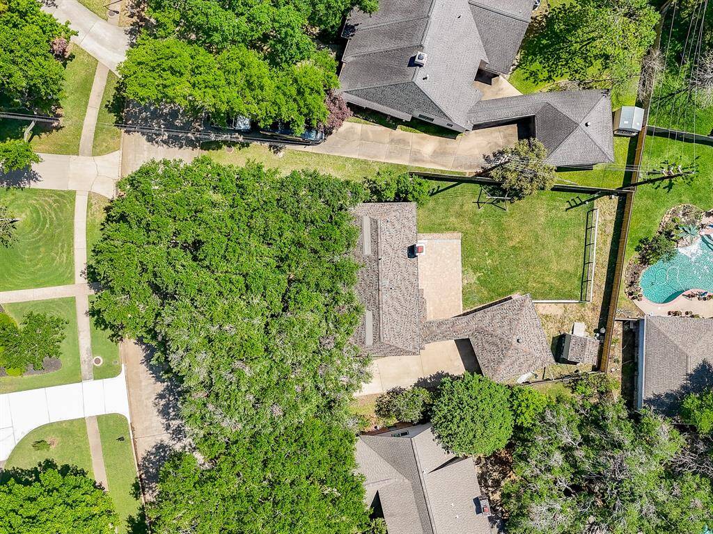 This aerial photo shows the home has a spacious backyard and a large patio area. The house is surrounded by greenery and is part of a neighborhood with similar properties. The backyard is fenced, offering privacy and space for outdoor activities.