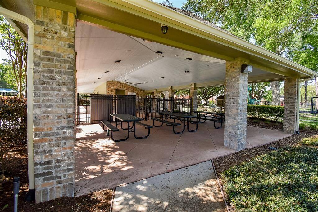 More amenities include: A covered outdoor pavilion with brick pillars and several picnic tables, ideal for gatherings. The space is surrounded by greenery, providing a pleasant and shaded environment.