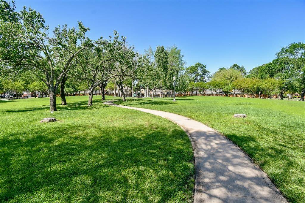 Enjoy the park setting with a winding pathway surrounded by lush green grass and mature trees, ideal for leisurely walks and outdoor enjoyment.