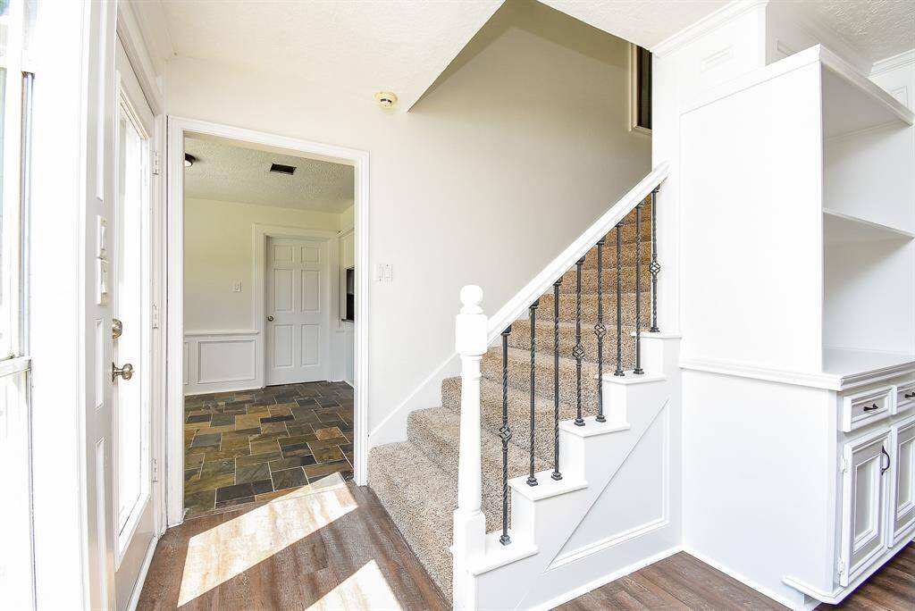 Bright entryway from the back door with natural light, featuring a carpeted staircase with decorative iron balusters.