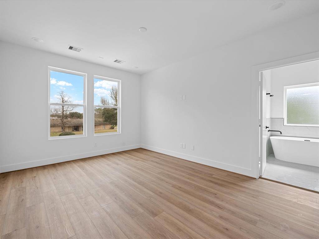 This photo showcases a bright, spacious bedroom with large windows, wood flooring, and an adjoining bathroom featuring a modern bathtub. Perfect for those seeking a contemporary and airy living space.