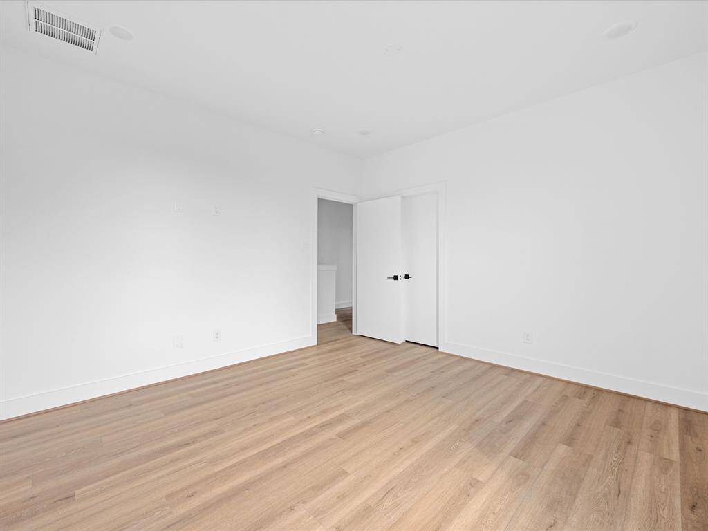 This photo shows a bright, empty room with white walls and light wood flooring. It features a modern feel with a simple, white door and ceiling vent. Ideal for a bedroom or home office.