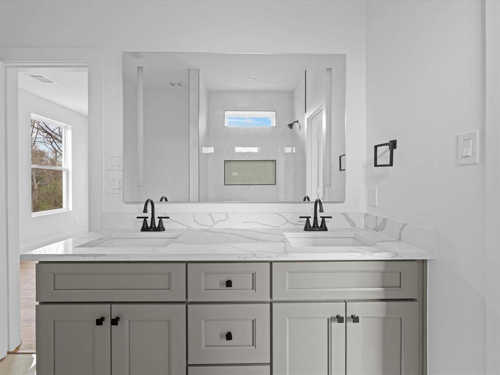 This bathroom features a modern double vanity with marble countertops, sleek black fixtures, and a large mirror. The space is bright and airy with a window offering natural light.