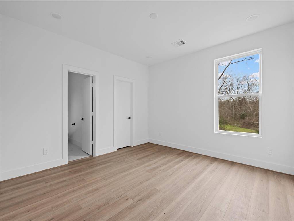 This bright, minimalist room features light wood flooring, two white doors, and a large window with a scenic view, offering a serene and modern living space.