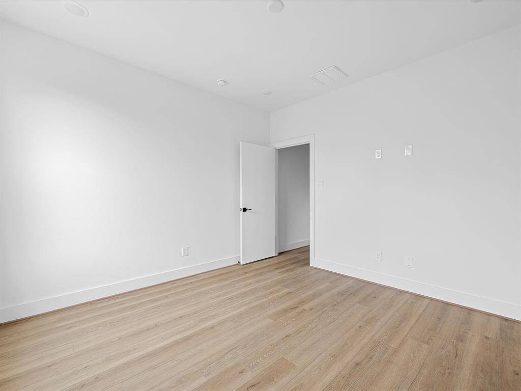 This photo shows a bright, empty room with light wood flooring and white walls. The room has a door leading to another space, creating a clean and modern look, perfect for customization.